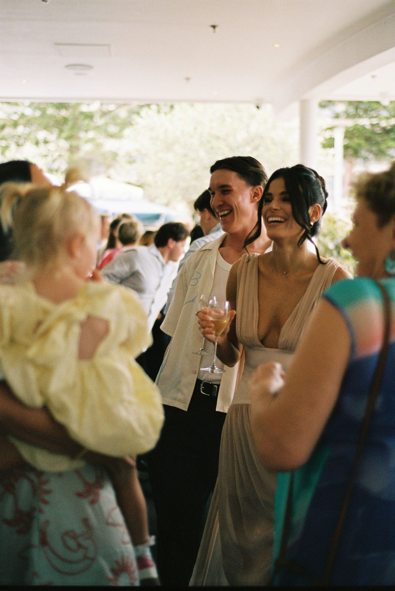Wedding guests dancing and laughing together at a reception celebration under white tent lighting.