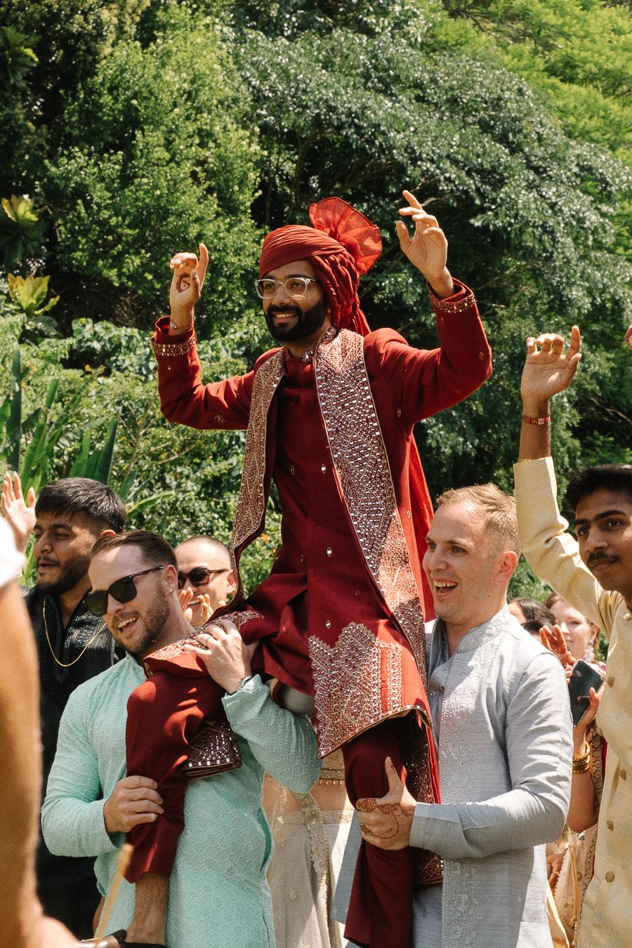A group celebrates outdoors with someone wearing a red velvet outfit and sparkly vest leading festivities in a garden setting.