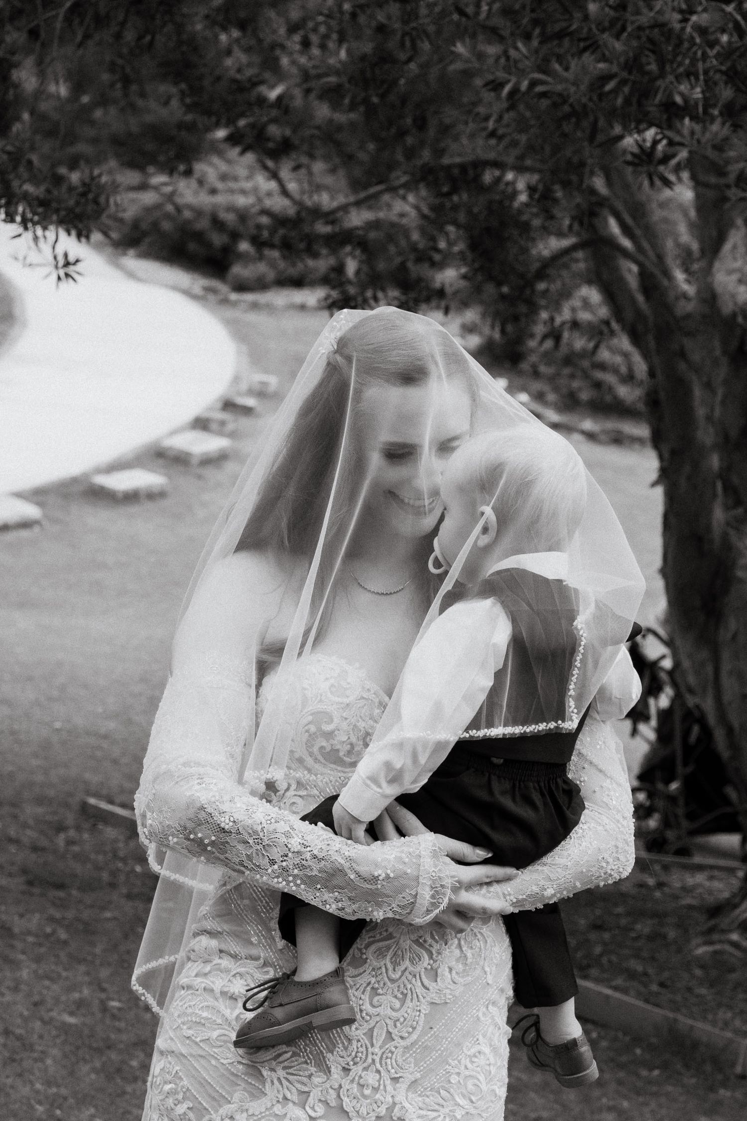 A romantic black and white wedding photo series showing a couple embracing under a delicate lace veil in a garden setting.