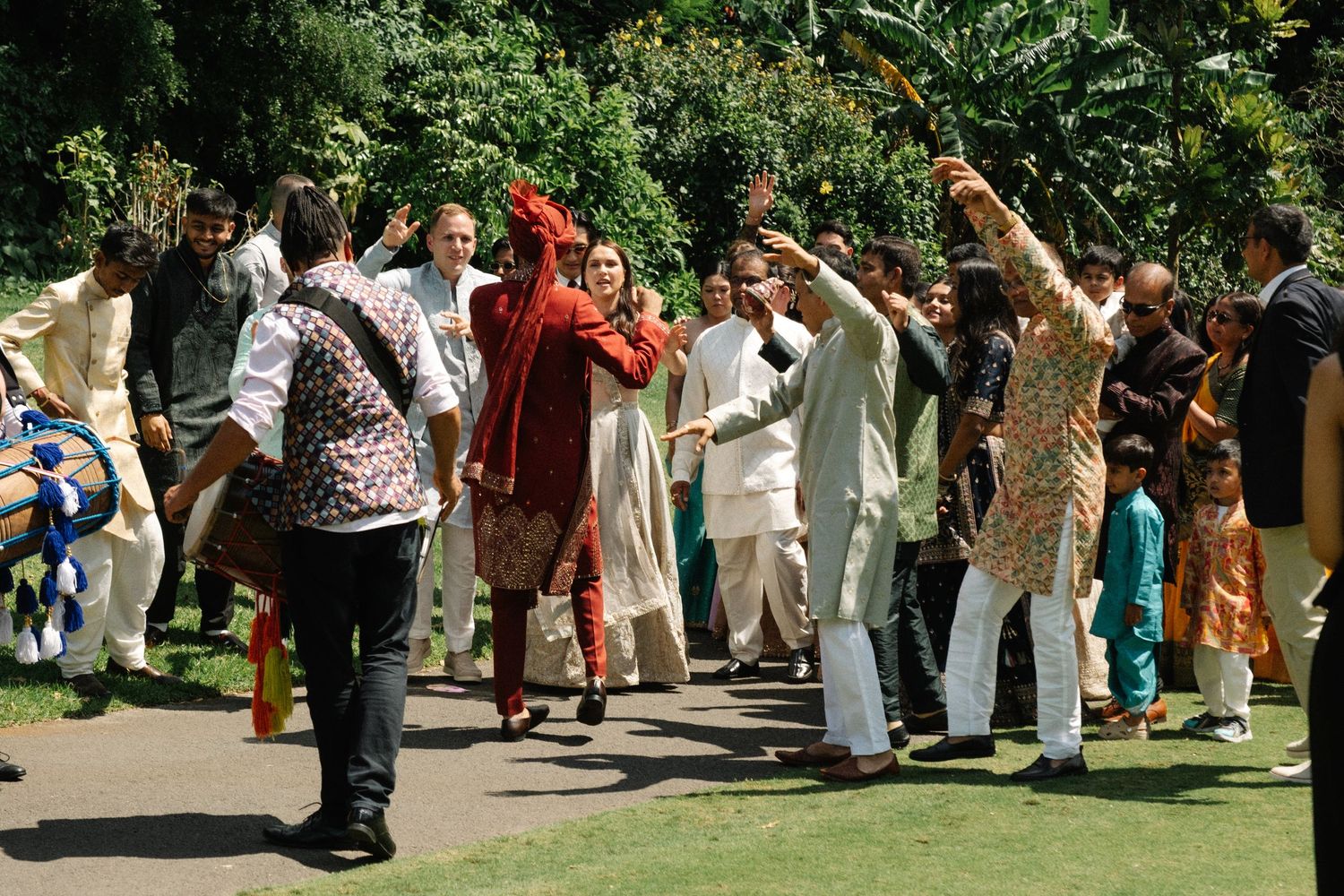 A group of people dancing together outdoors in a garden setting on a sunny summer day.