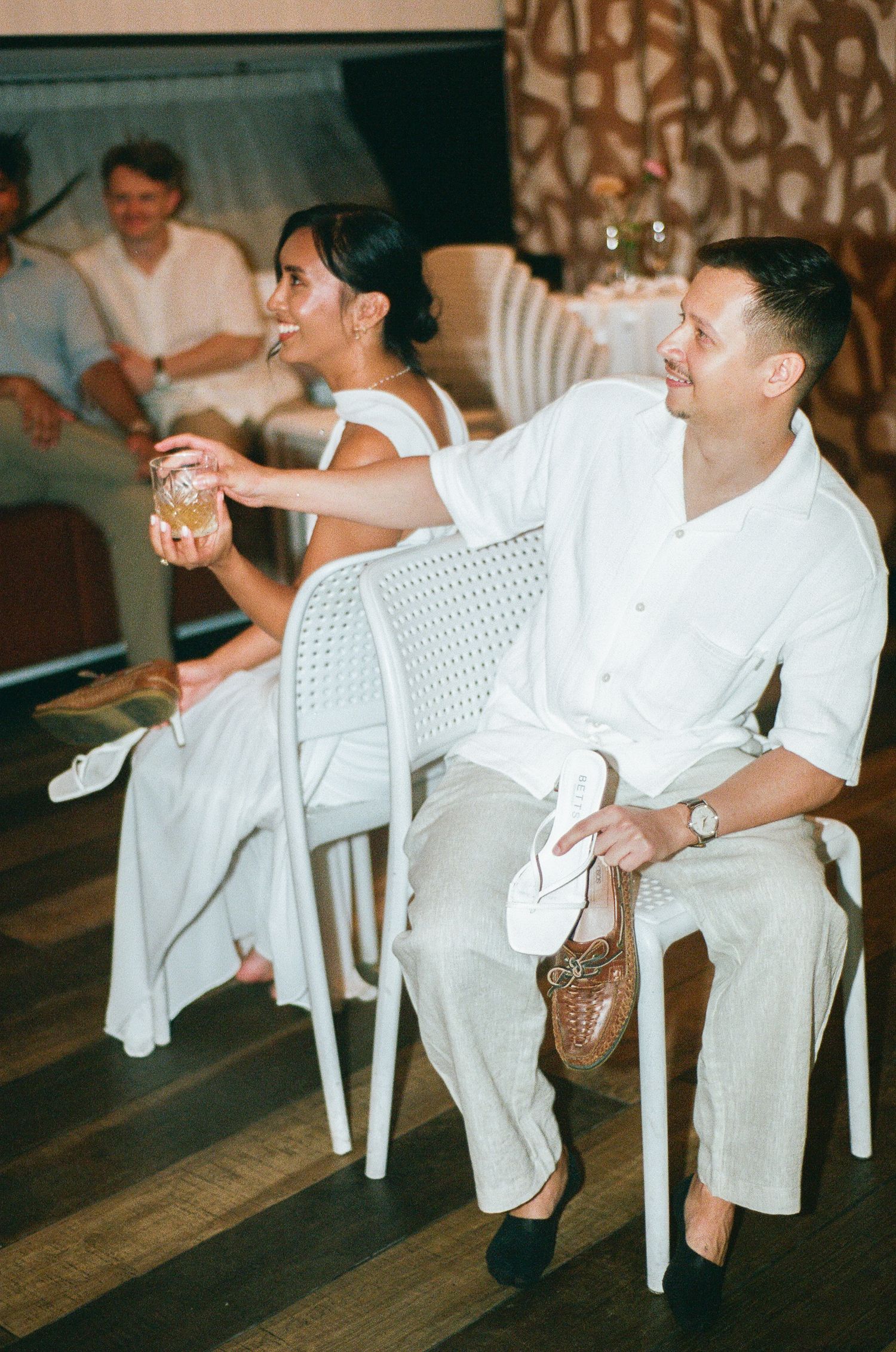 People in white clothing sit in plastic chairs during a casual gathering or event.