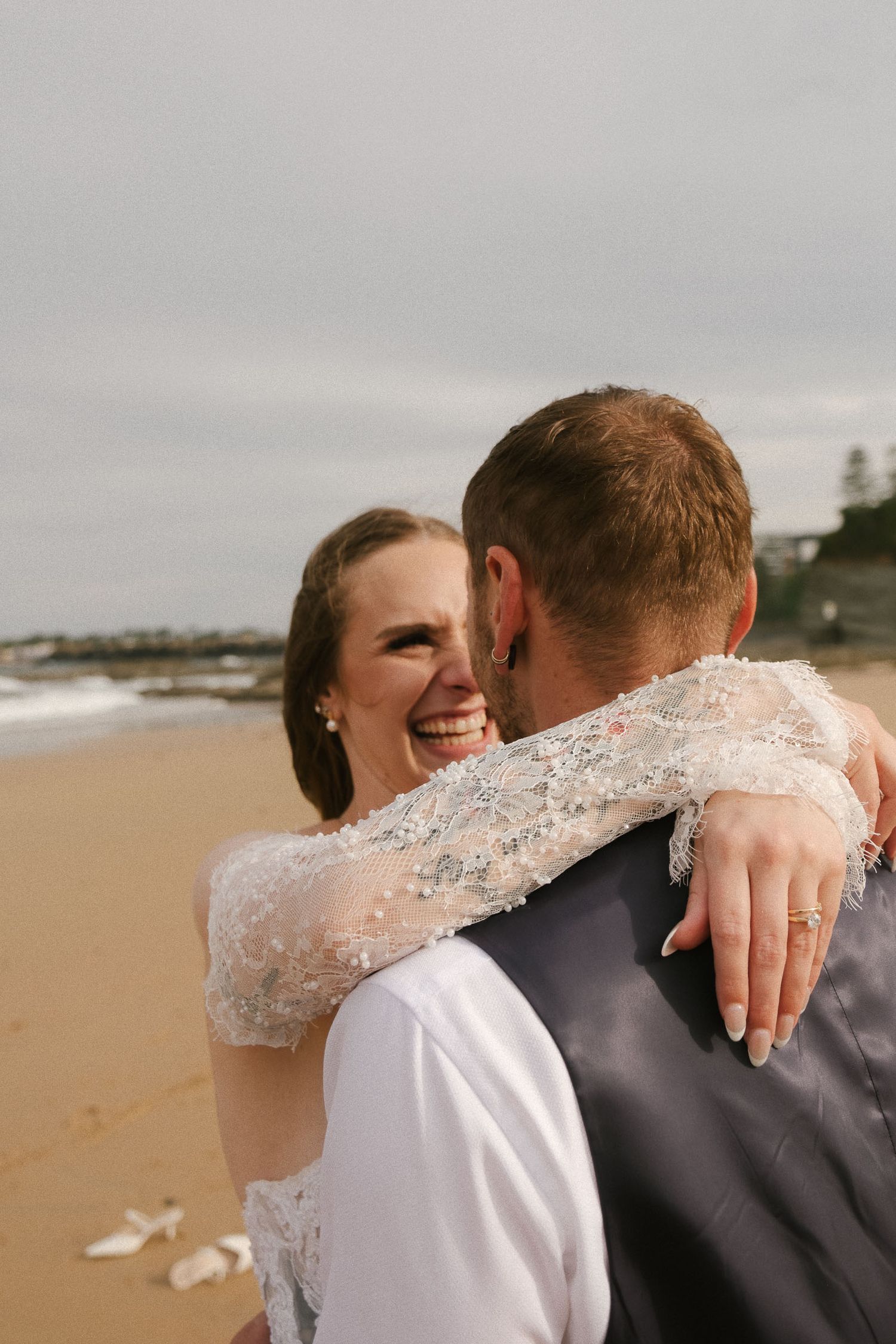 A happy couple embraces on a cloudy beach during their wedding celebration.
