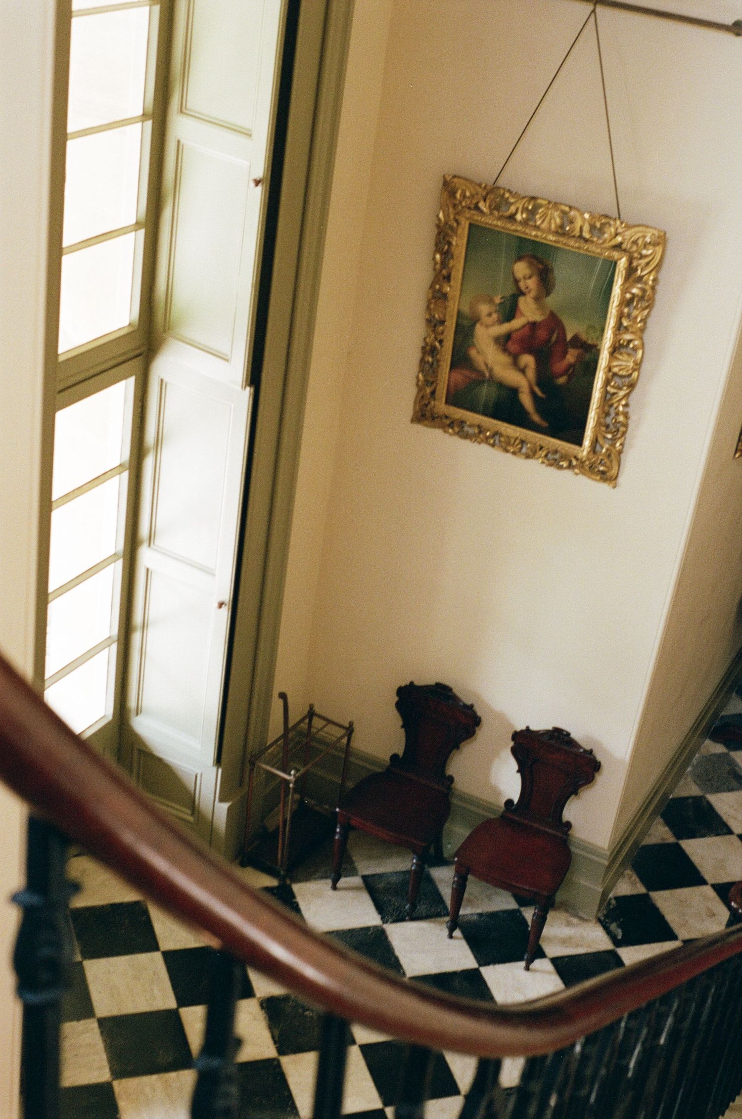 Elegant curved wooden banister and black and white checkered floor in a historic interior with ornate framed artwork.