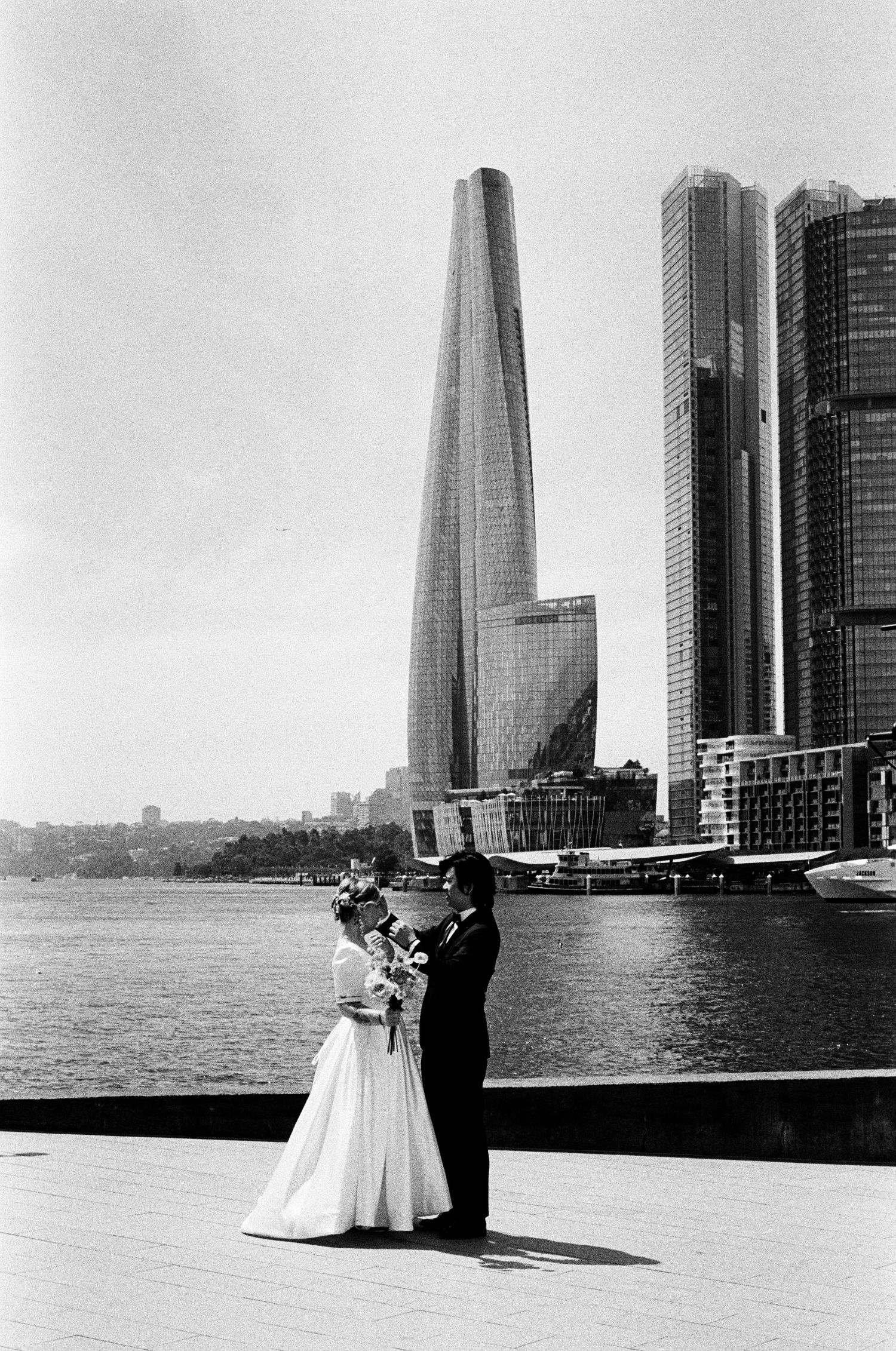 A black and white wedding photo series showing a couple against a backdrop of modern city skyscrapers by the waterfront.