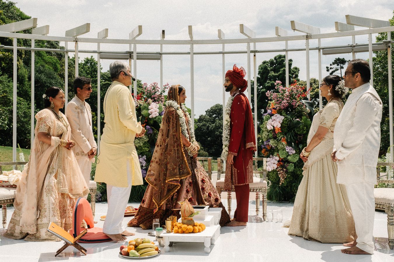 Traditional Indian wedding ceremony taking place under a white pergola with guests in elegant ethnic attire and food platters.
