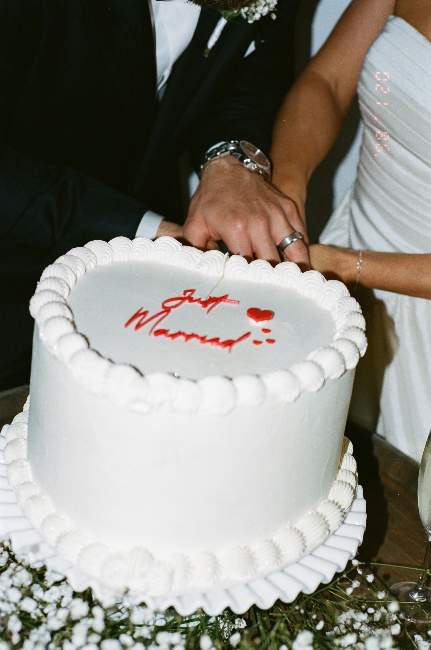 Couple in wedding attire cutting a white frosted cake with red 