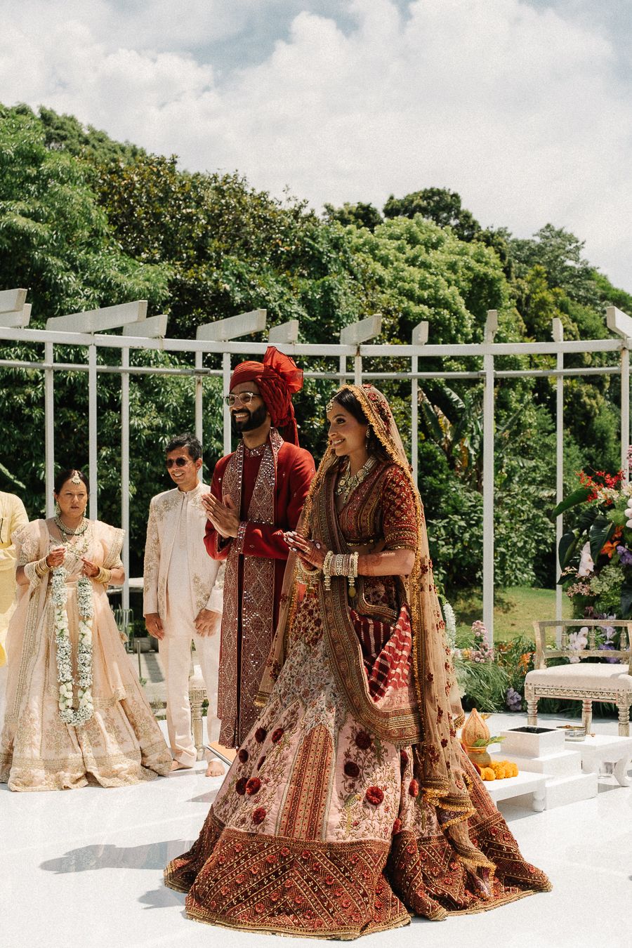 Traditional South Asian wedding attire and bridal lehengas displayed on hangers against white outdoor railings.