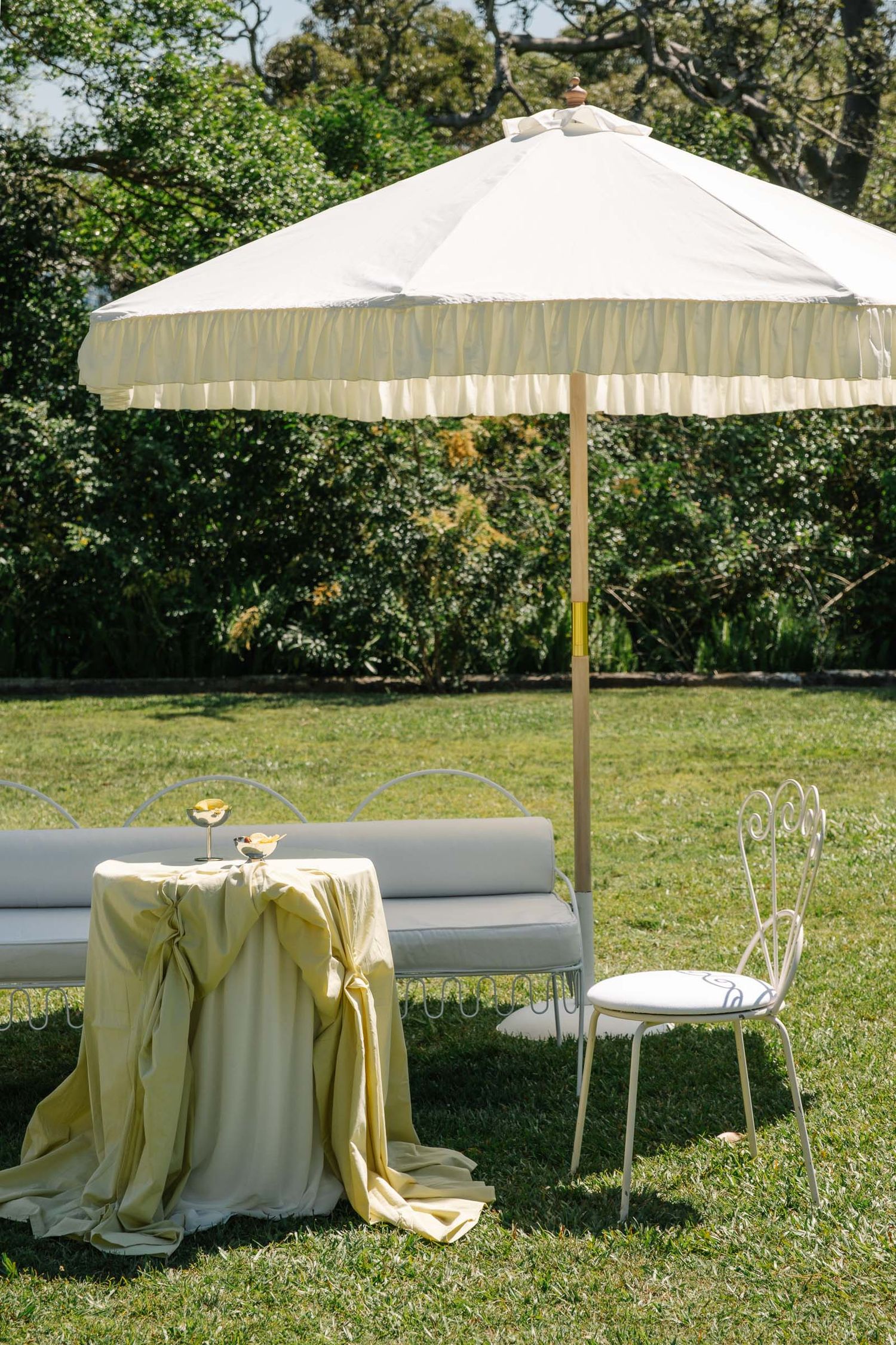 White patio umbrellas with cream tablecloths set up on a sunny lawn for an outdoor event.