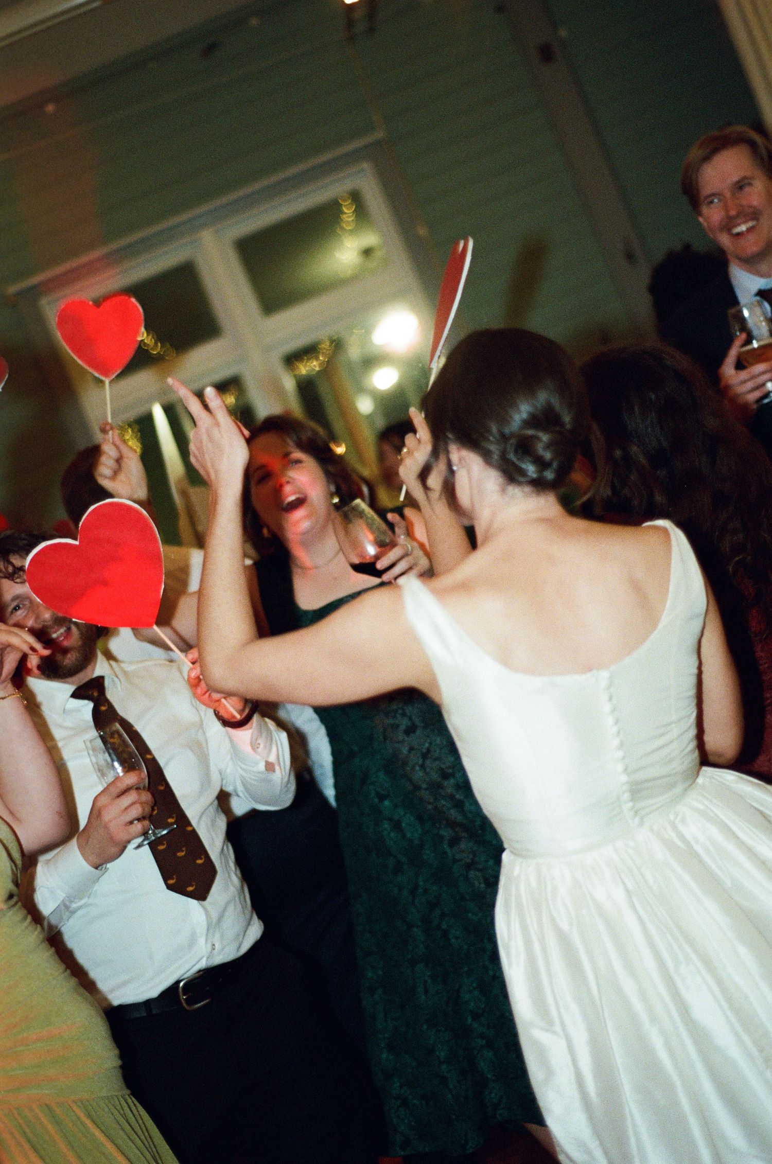 Bride dancing with guests holding red heart props at colorful wedding reception celebration.