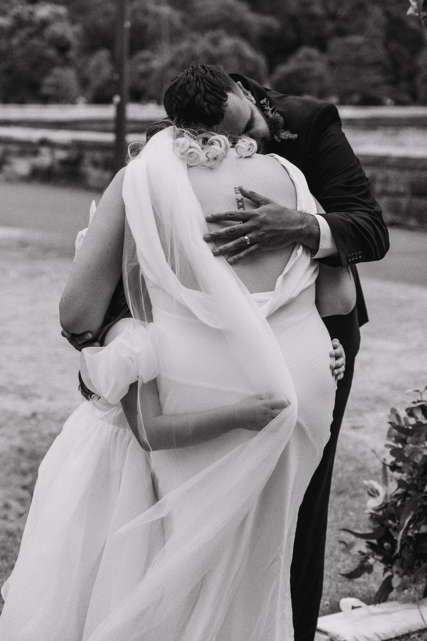 A romantic black and white wedding photo showing a passionate embrace with the bride's white veil flowing in the breeze.