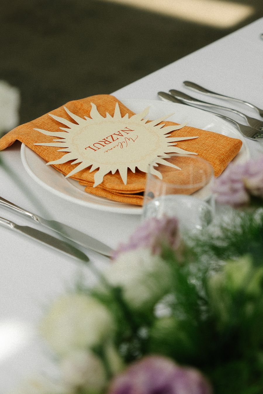 A blurred orange menu card or paper with text lies on a table with soft focus flowers in the foreground.