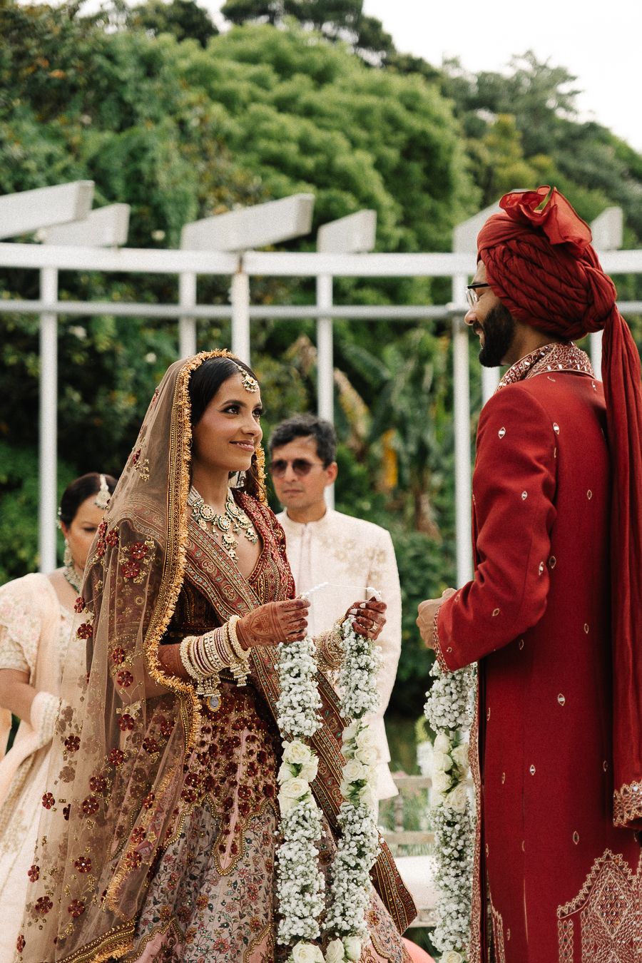 A couple in traditional South Asian wedding attire standing together during an outdoor ceremony.