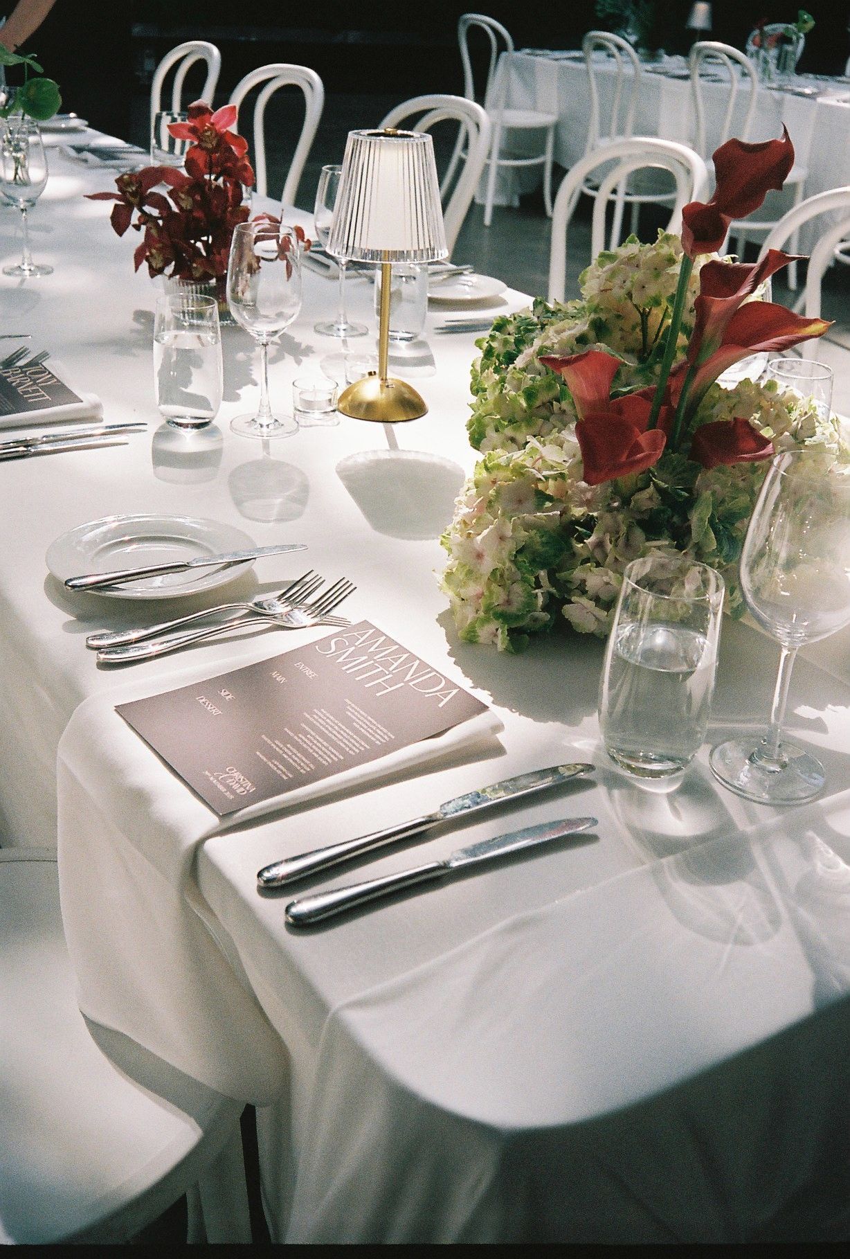 Elegant white table settings with silverware and glassware arranged on crisp white tablecloths for a formal dining event.