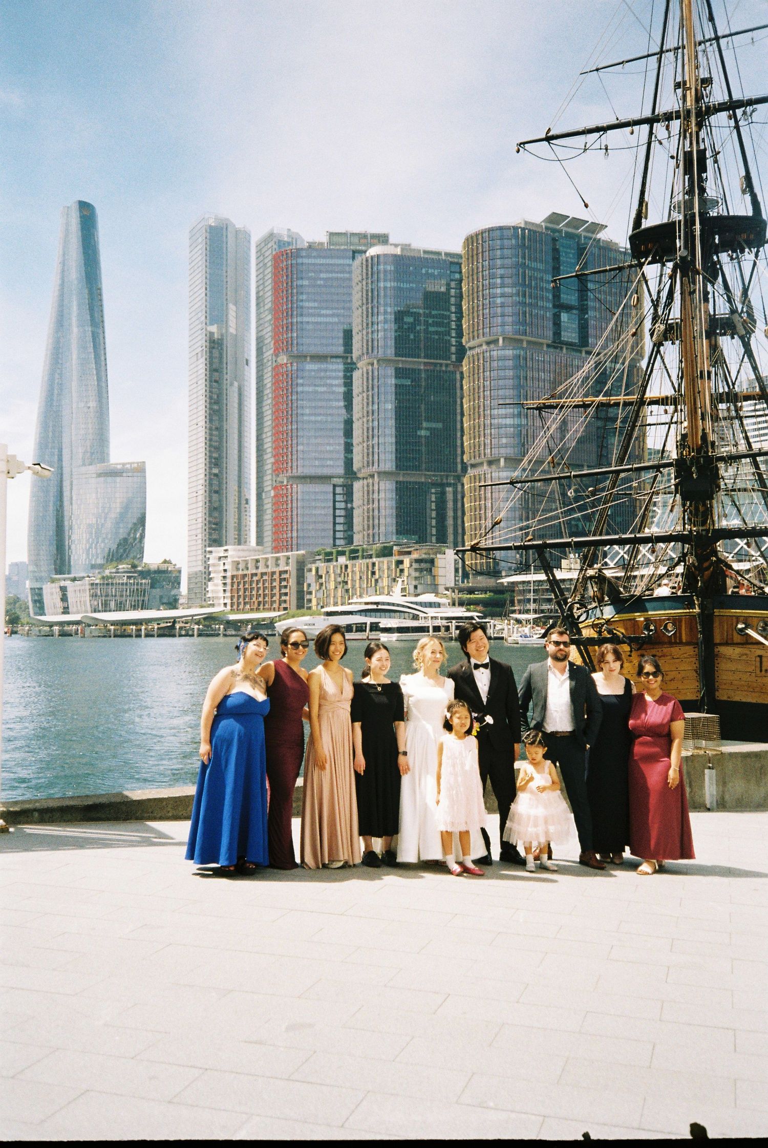 A group in formal attire poses by a historic ship with modern skyscrapers and the Shanghai Tower in the background.