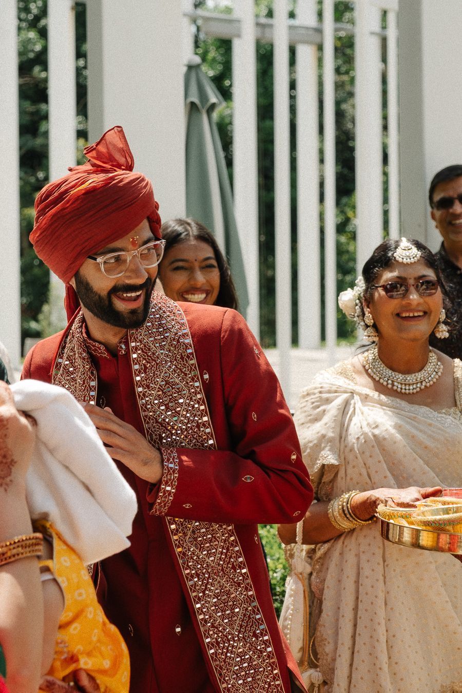 Group of wedding guests in traditional Indian attire laughing and celebrating at an outdoor venue.