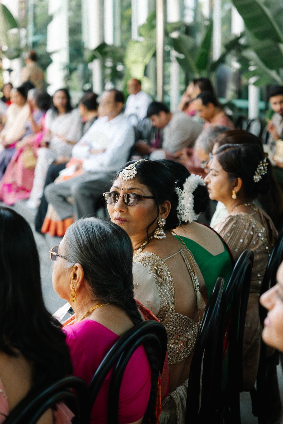 Guests in traditional Indian attire seated at a formal event with decorative pillars and greenery in the background.