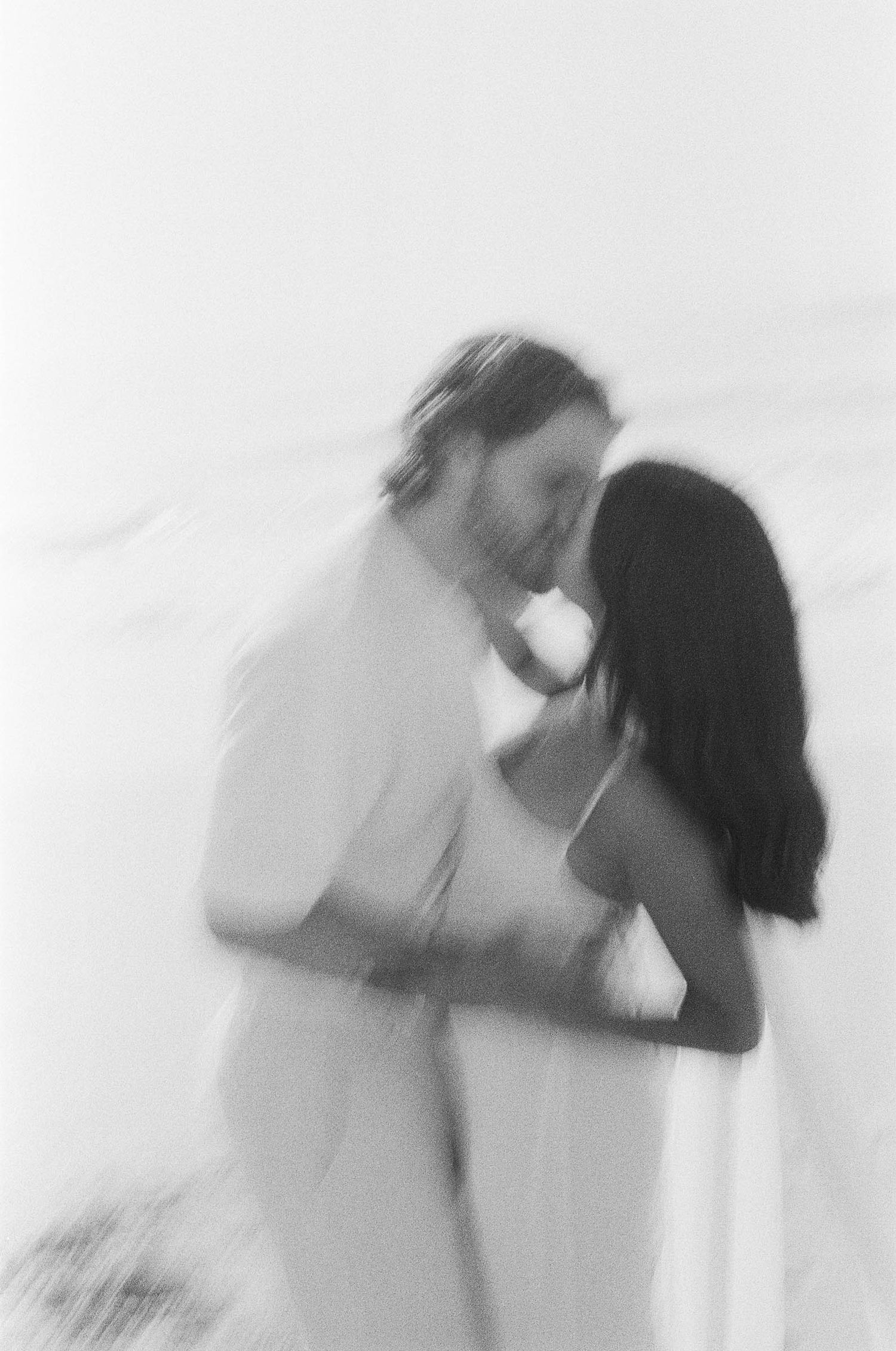 A soft, dreamy black and white photo of a couple sharing a romantic kiss in ethereal lighting.