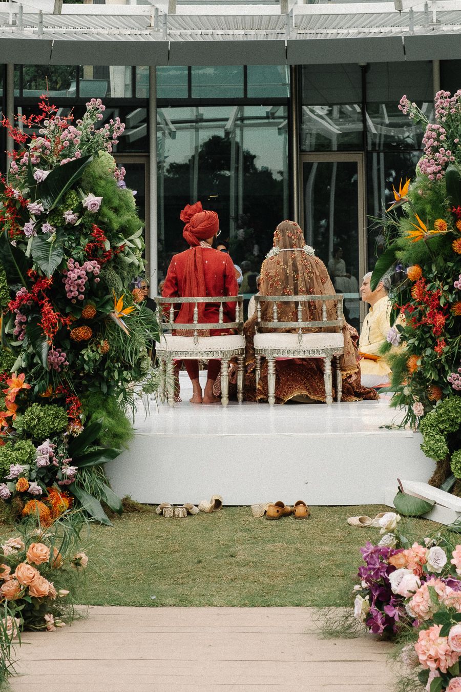 Outdoor wedding ceremony setup with wooden chairs and vibrant floral arrangements along a grass aisle.