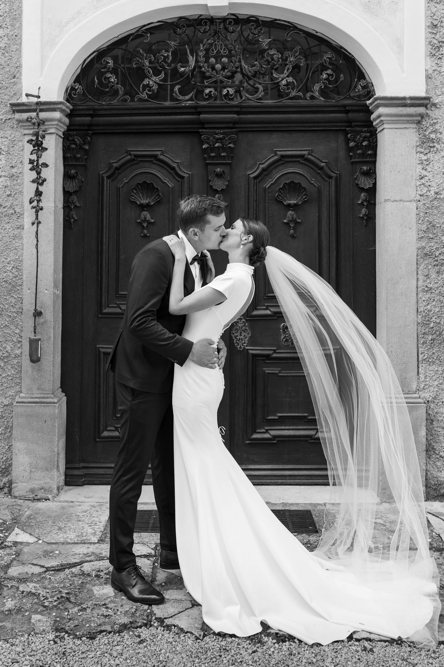 A romantic wedding couple embraces in front of ornate black doors in a series of black and white photographs.