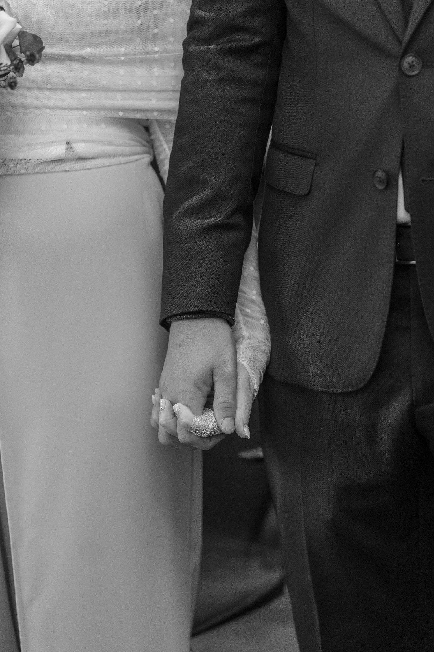 Black and white close-up photo of a couple holding hands during a wedding ceremony.