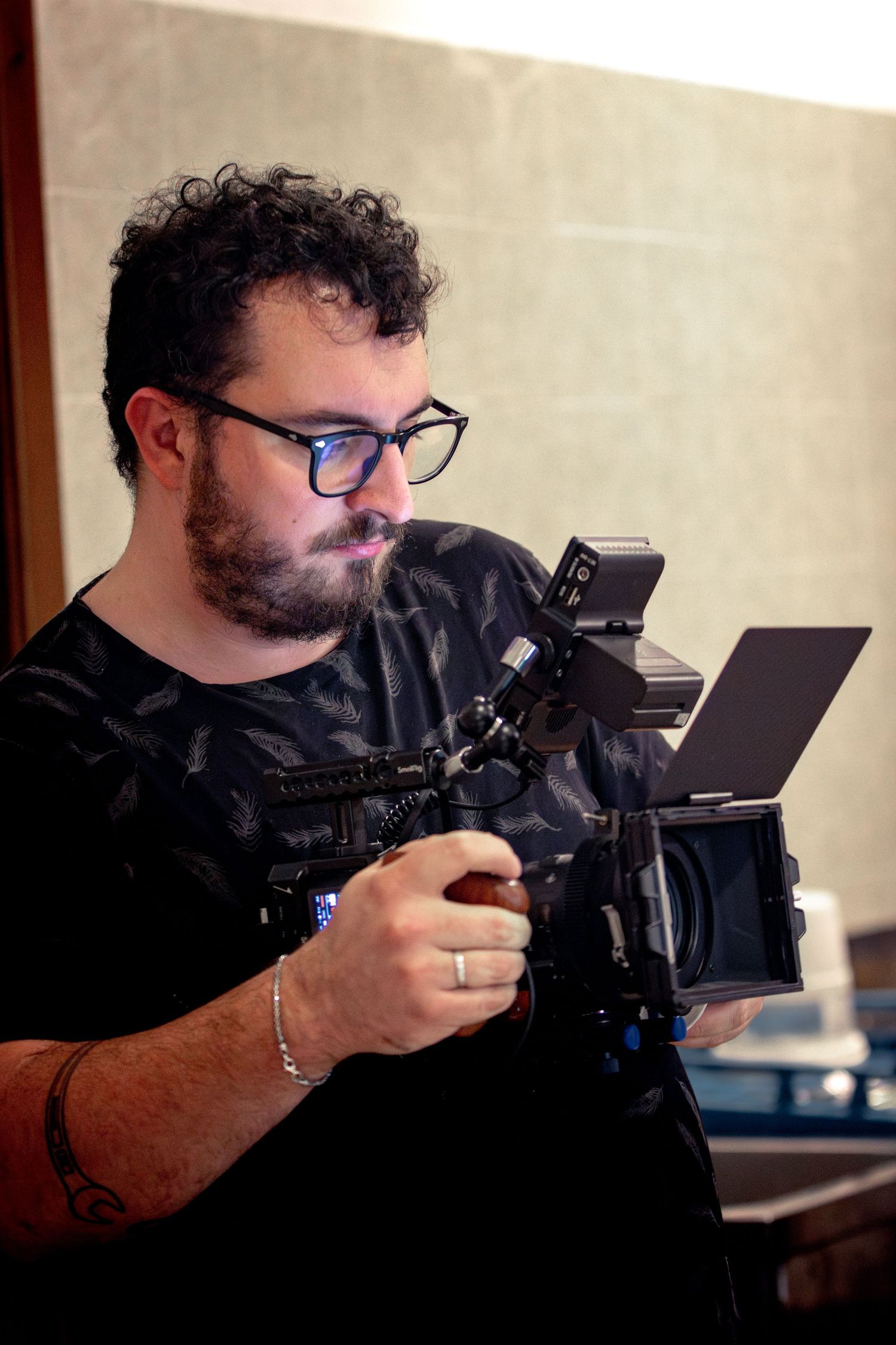 Bearded man with glasses operating a professional video camera rig on set.