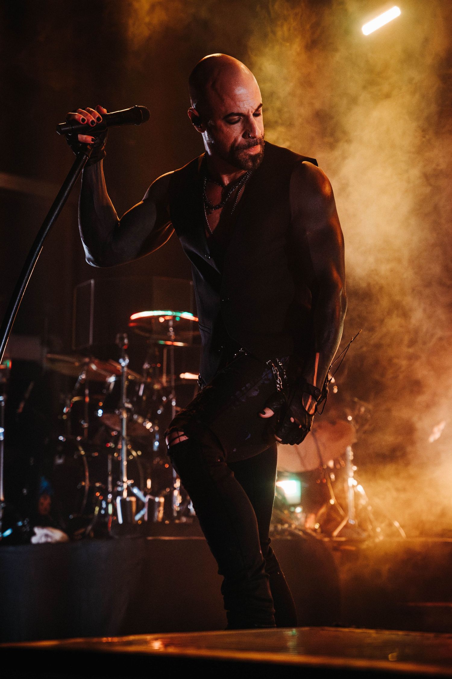 A performer sings on a dimly lit stage with atmospheric smoke effects and dramatic backlighting creating a moody ambiance.