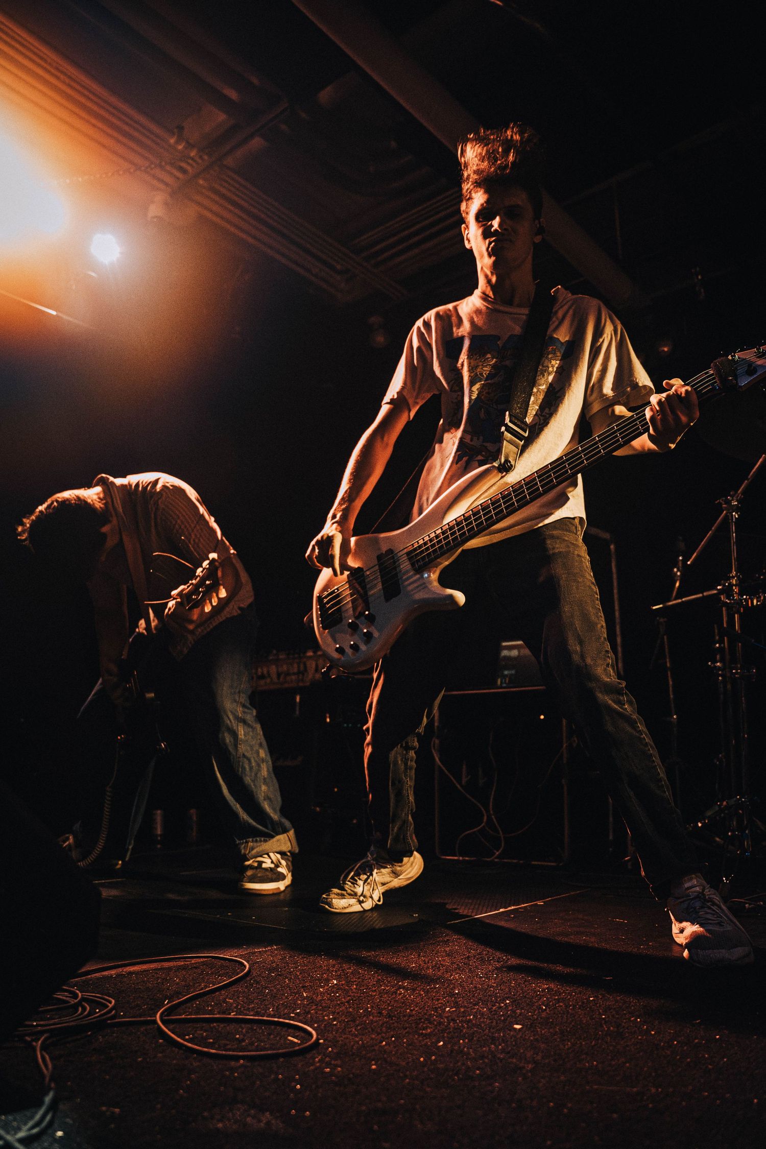 Musicians perform energetically on a dimly lit stage during a rock concert with dramatic lighting and movement.