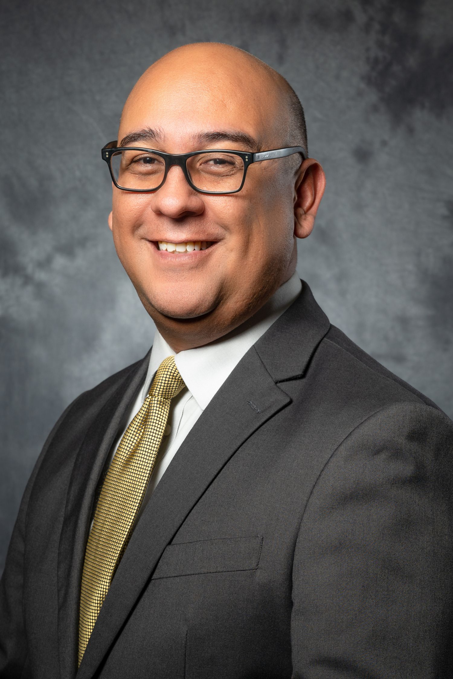 Professional headshot series showing a person in a dark suit and gold tie against a gray background with varying expressions.