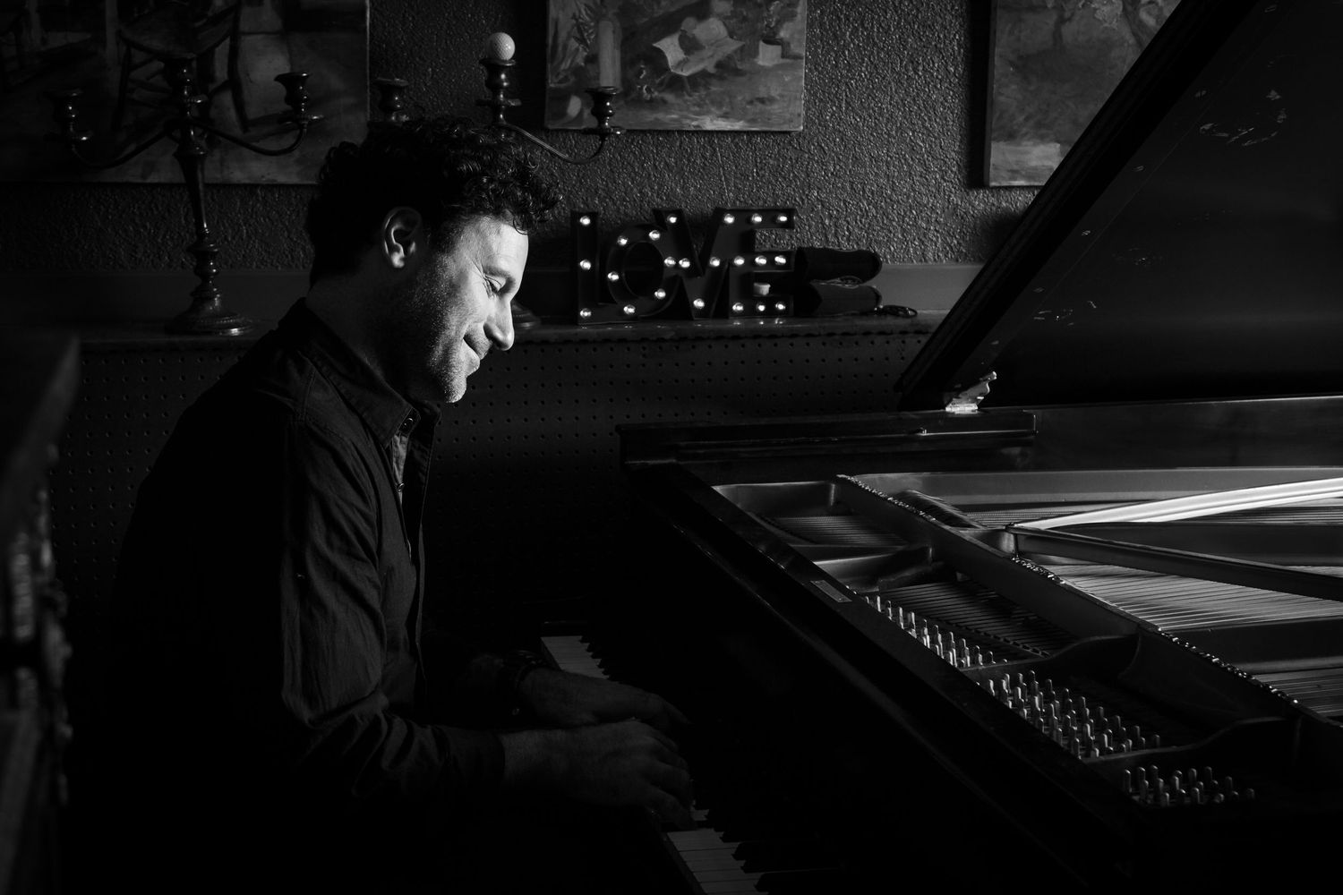Black and white photo of a pianist performing at a grand piano in a dark concert setting.