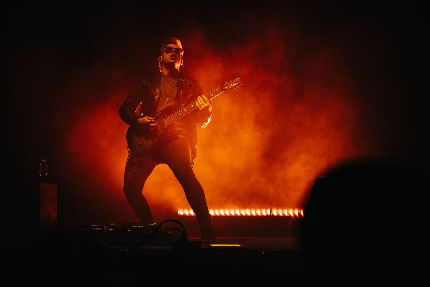 A silhouetted figure performs on a concert stage bathed in dramatic orange and red lighting effects.