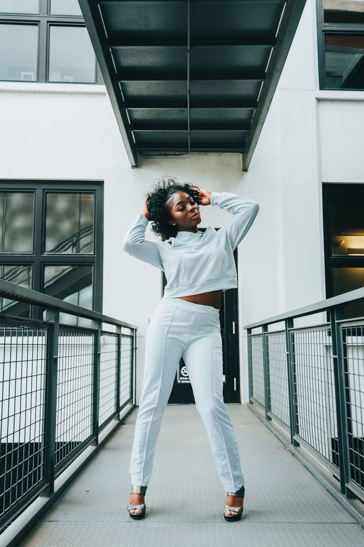 A person in an all-white outfit strikes a dynamic pose on a modern walkway with metal railings and architectural details.