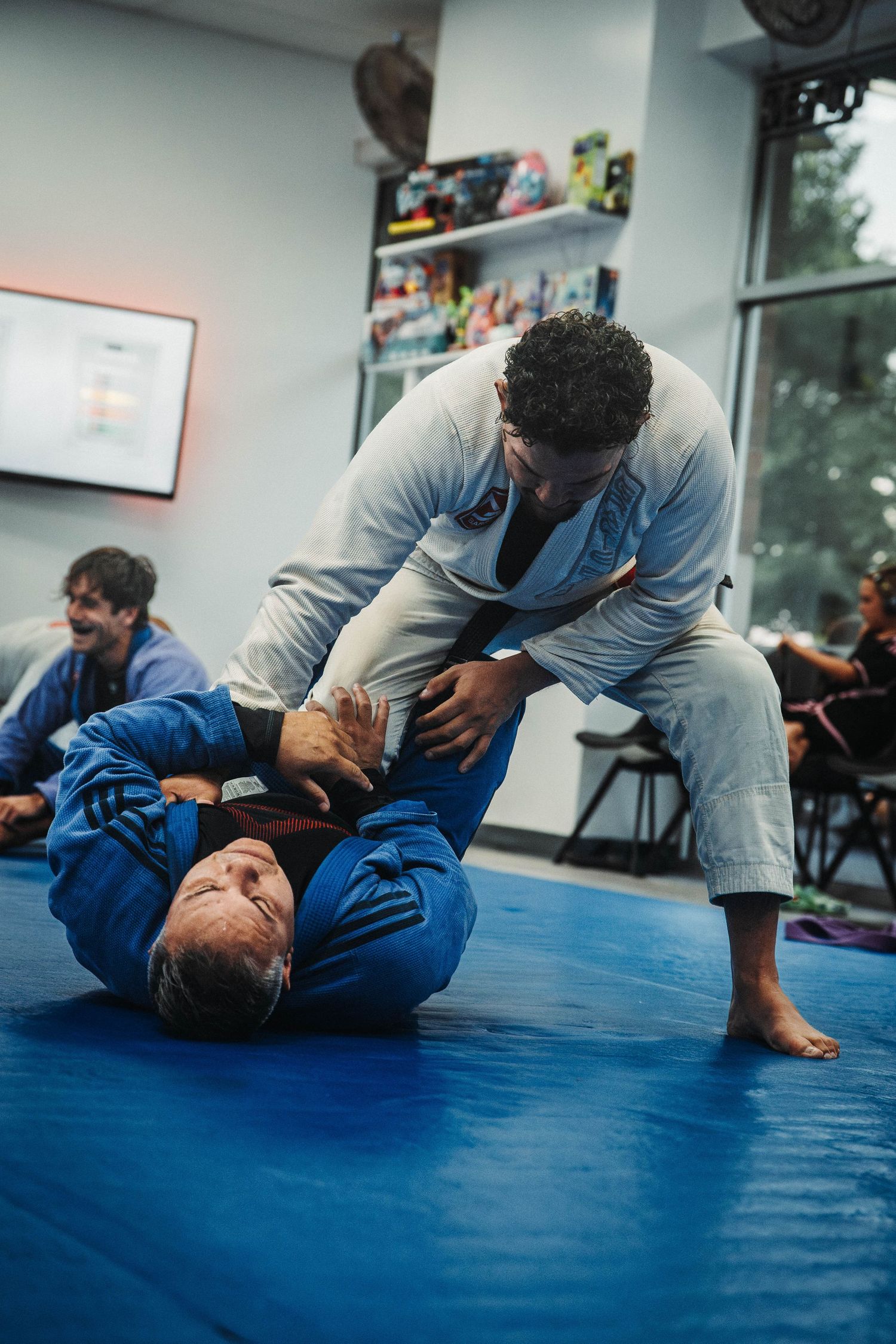 Two martial artists practicing Brazilian Jiu-Jitsu grappling techniques on blue training mats.