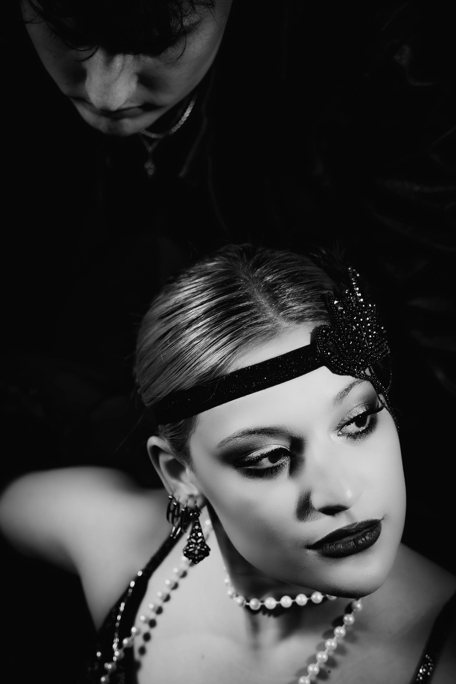 Black and white glamour portrait with dramatic lighting, pearl necklace and dark lipstick creating a vintage aesthetic.