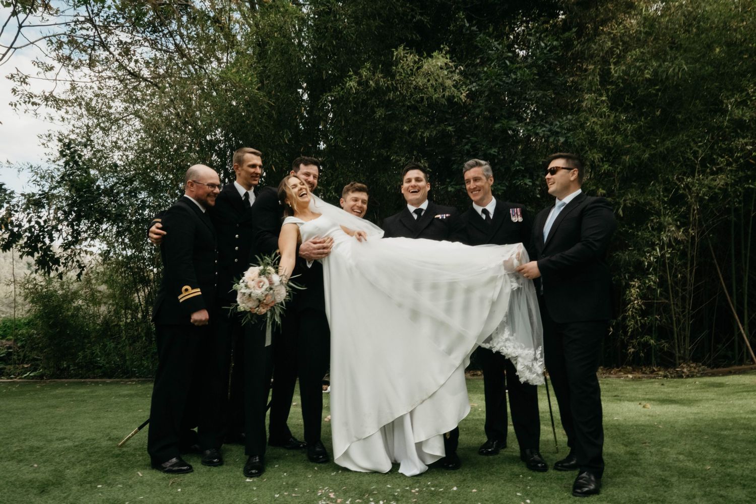 Bride lifted by groomsmen in naval uniforms at outdoor wedding venue near Barcelona