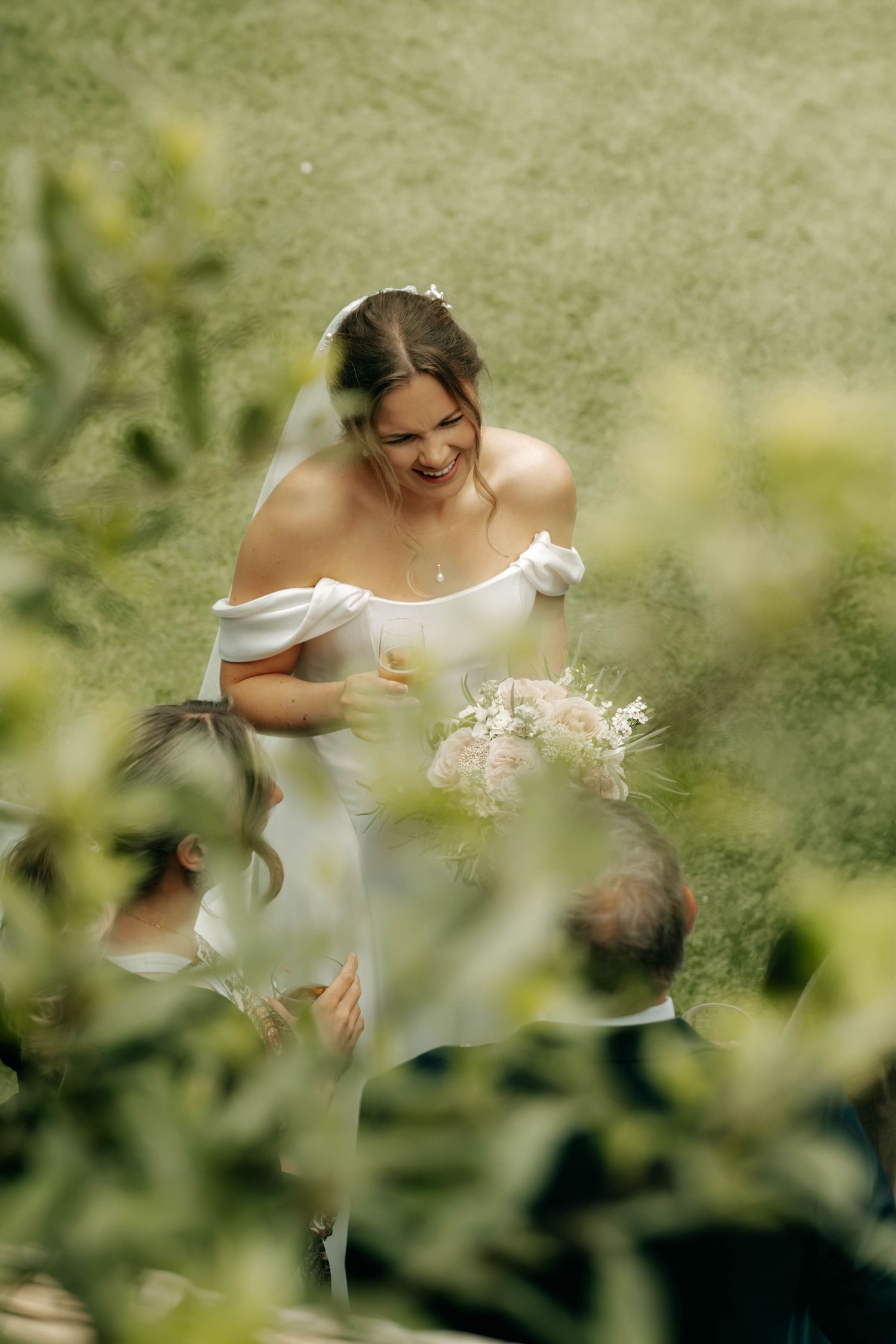 Candid moment of laughing bride captured through foliage, documentary wedding photography Spain