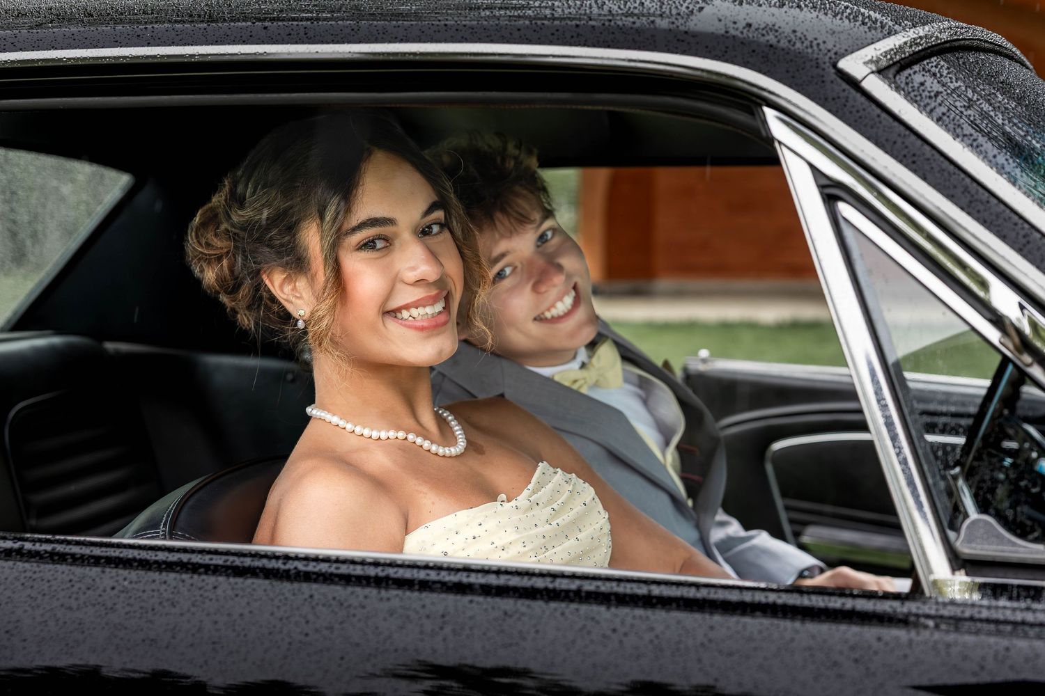 Smiling bride and groom sitting in a classic black car on their wedding day.