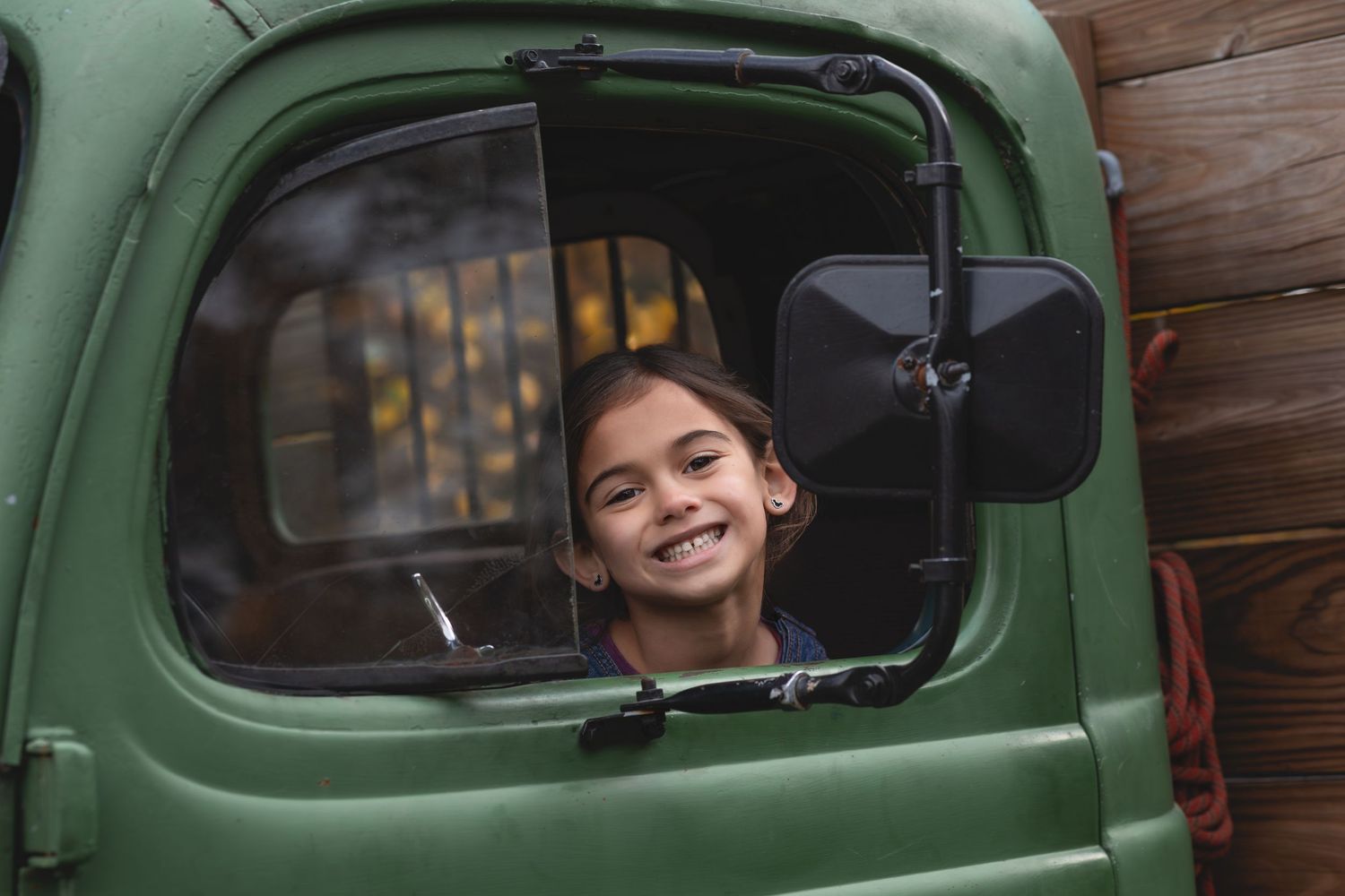 Smiling young girl peering out the window of a vintage green truck.