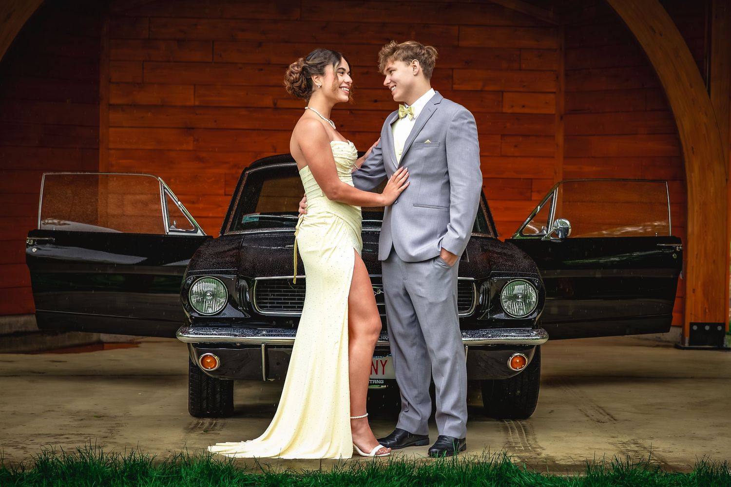 Bride and groom posing in front of a classic black Ford Mustang at a rustic barn wedding venue.