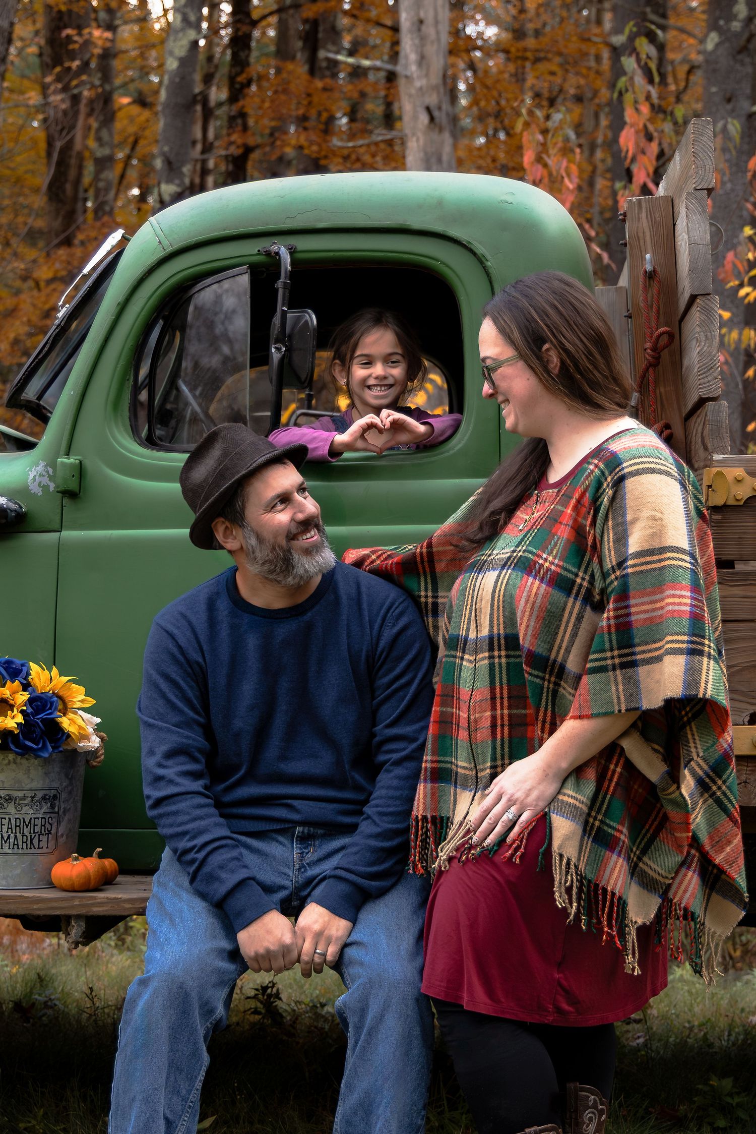 Smiling family shares a tender moment by a vintage green truck as child peeks from window.
