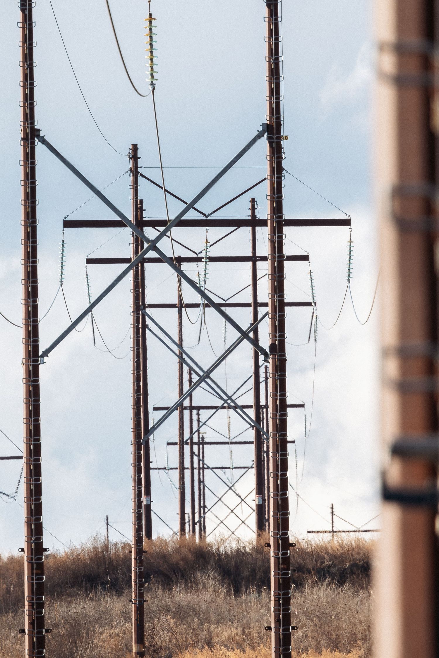 Rusty steel electrical transmission towers and wooden utility poles with power lines against a partly cloudy sky.