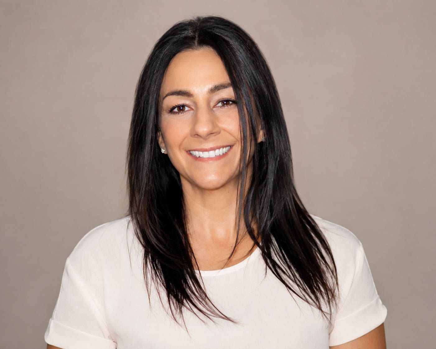 Professional headshot of a smiling woman with long dark hair wearing a white top against a gray background.
