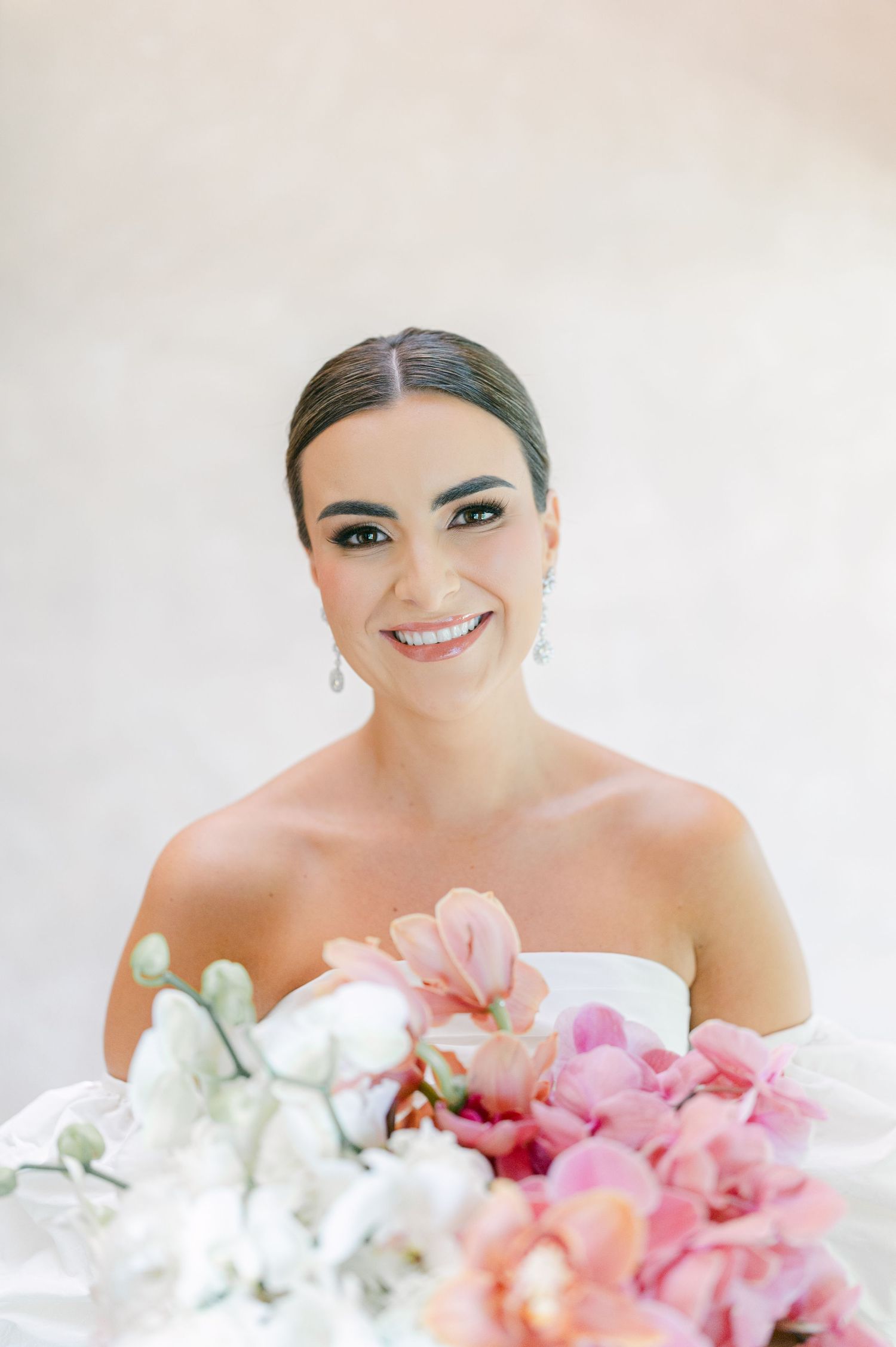 Smiling bride with sleek updo holds colorful pink and white orchid bouquet in strapless white wedding gown.