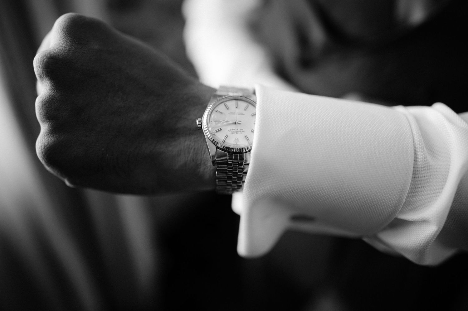 Close-up black and white photo of groom adjusting classic silver wristwatch on wedding day.