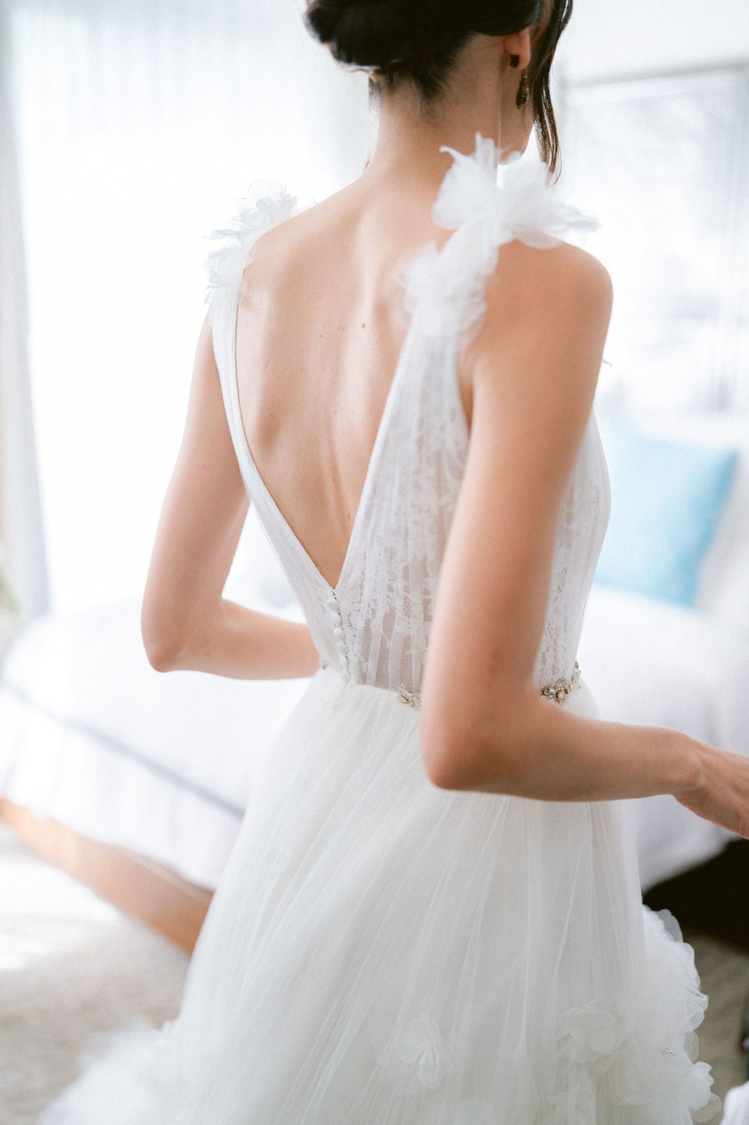 Elegant backless wedding gown with feather shoulder details and deep V-back on bride.