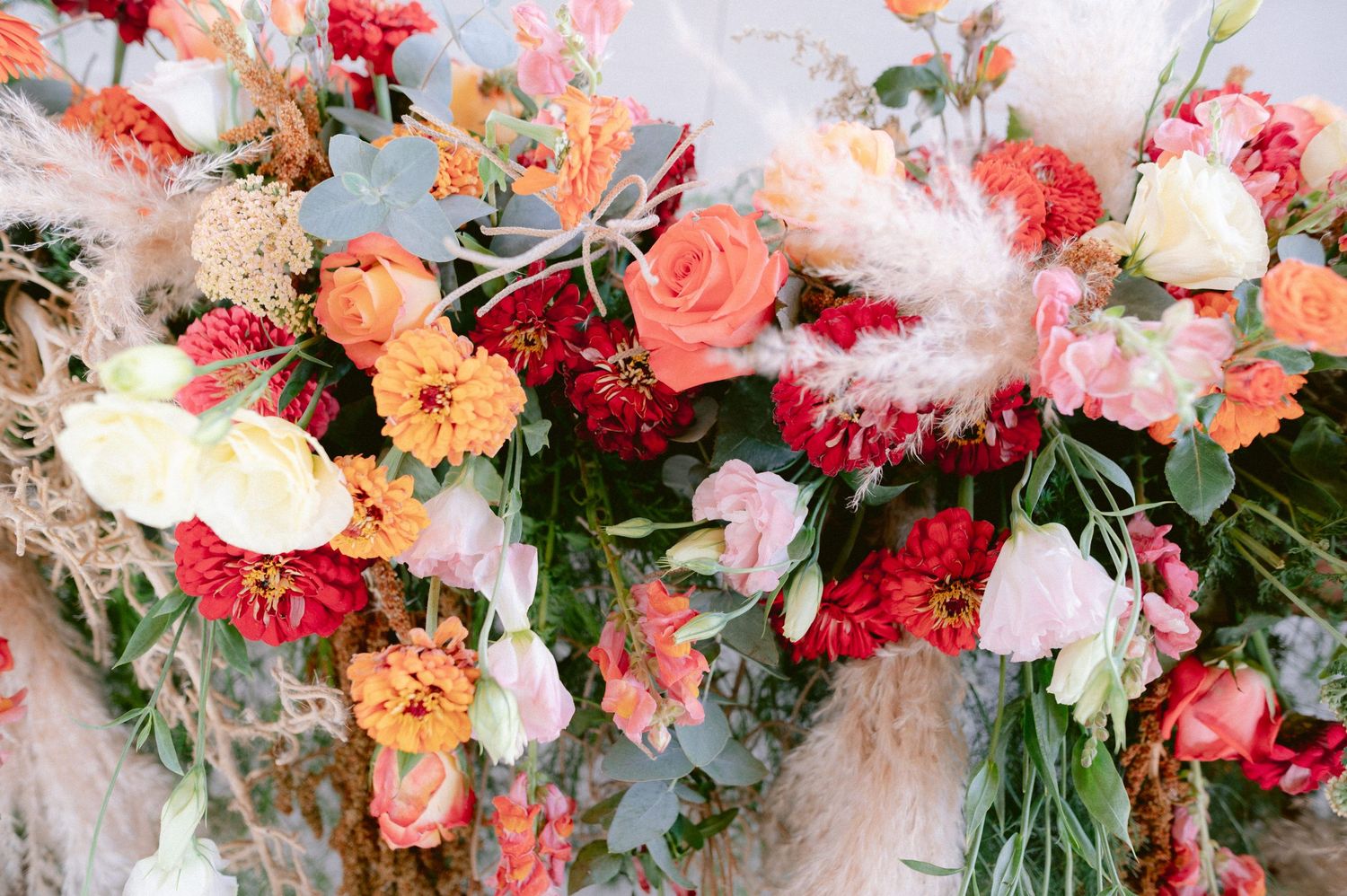 Lush wedding floral arrangement featuring orange, red, pink roses and pampas grass accents.