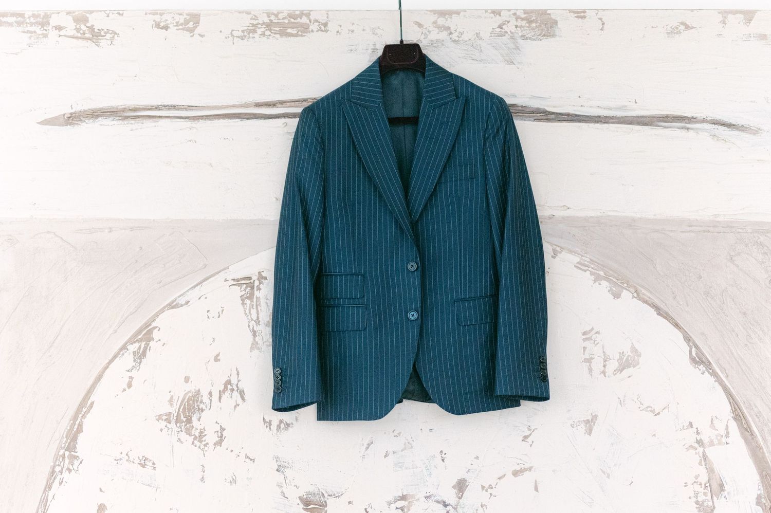 Teal pinstripe blazer with two buttons hanging on a hanger against a white distressed wall background.