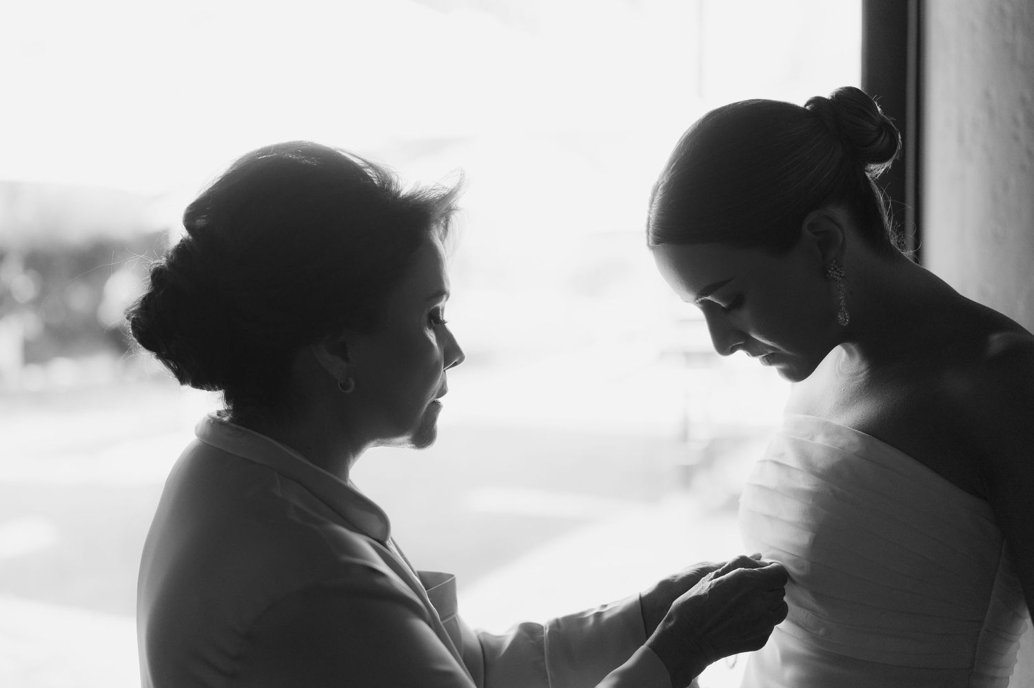 Black and white photo of two women sharing a tender moment by a bright window.