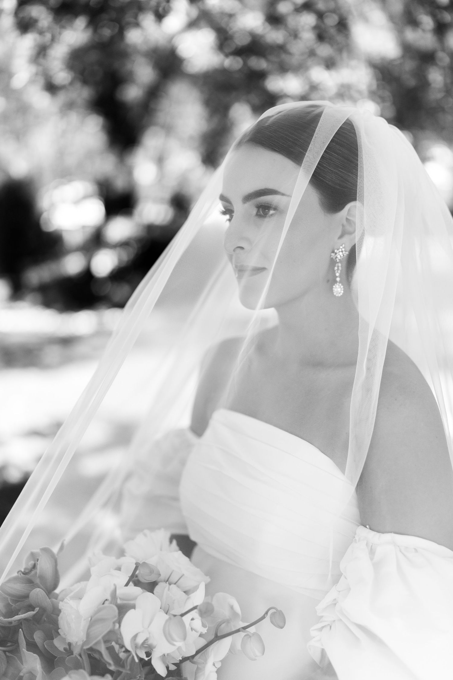 Stunning black and white bridal portrait with veil, drop earrings, and floral bouquet.