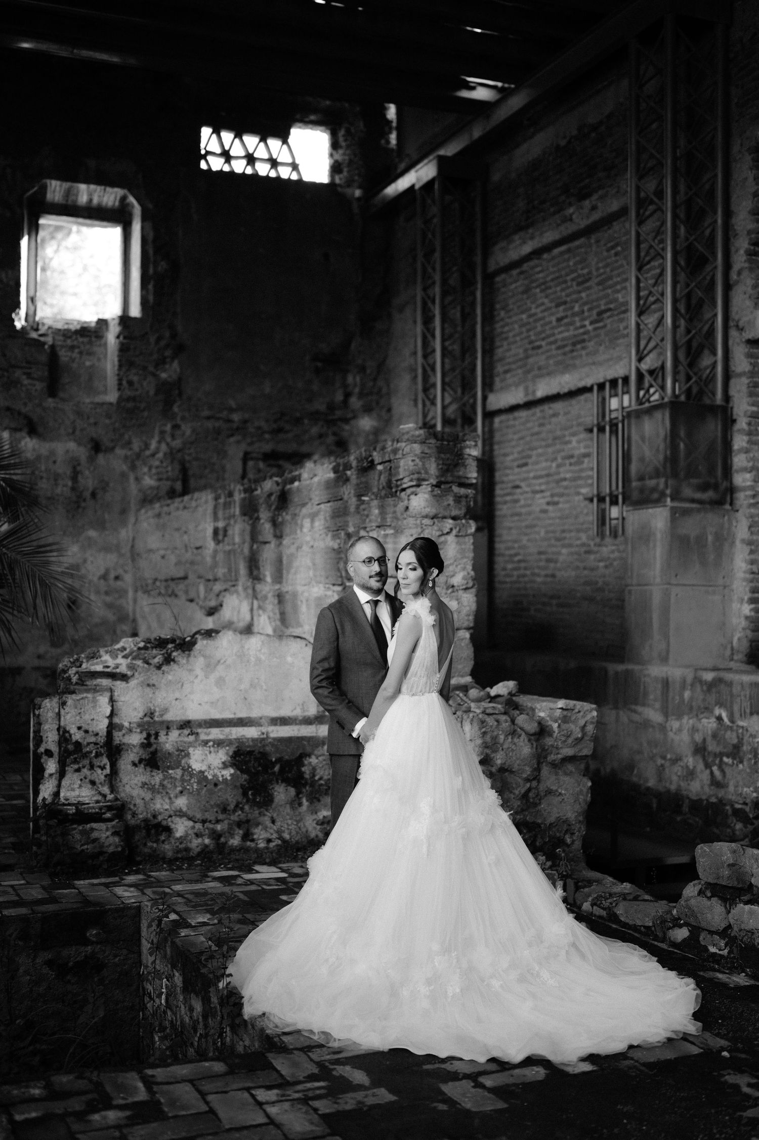 Black and white portrait of bride and groom embracing inside dramatic ancient brick ruins wedding venue.