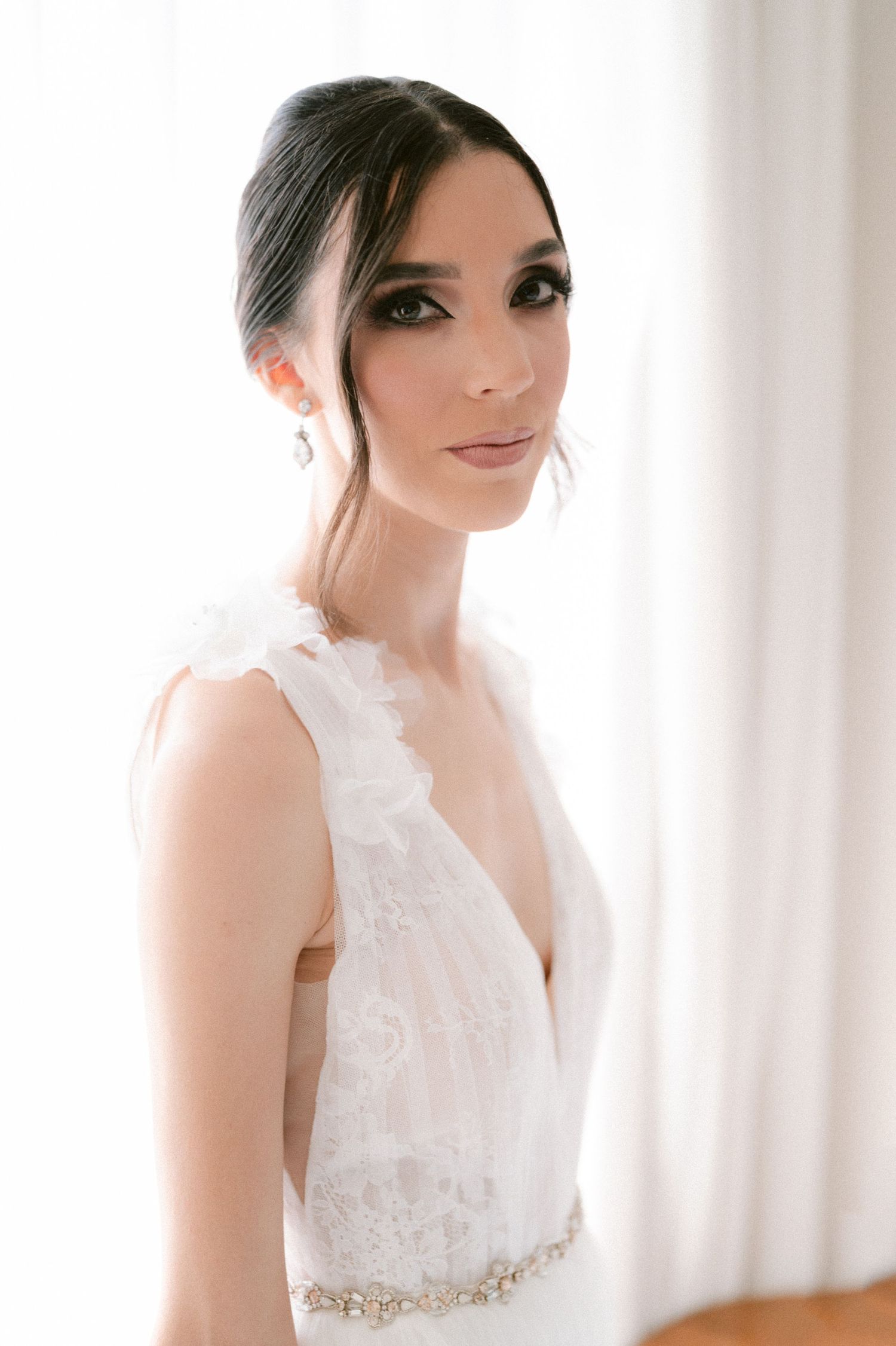 Close-up portrait of bride in lace V-neck gown with crystal belt in soft light.